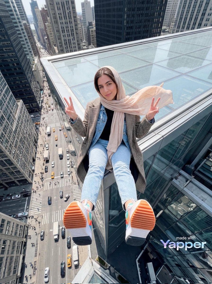 { "image_generation": { "subject": { "description": "young woman sitting at the edge of a skyscraper rooftop with a dramatic city view below", "pose": "sitting with legs extended toward the camera, both hands raised making peace signs", "expression": "playful confident smile", "gaze": "looking directly at the camera" }, "appearance": { "hair": { "color": "dark brown", "style": "covered with a light beige headscarf flowing in the wind" }, "skin": { "tone": "fair natural skin tone", "texture": "smooth realistic skin" }, "makeup": "light natural makeup" }, "outfit": { "outerwear": "long patterned coat", "inner_layer": "black top with denim jacket", "bottom": "light blue jeans", "footwear": "colorful sneakers with orange soles" }, "environment": { "setting": "urban city high-rise rooftop", "background_elements": [ "busy city street far below", "cars and taxis on the road", "tall buildings on both sides", "glass rooftop surface" ], "time_of_day": "daytime" }, "lighting": { "type": "natural daylight", "direction": "soft overhead light", "effect": "bright urban lighting with balanced shadows" }, "camera": { "angle": "extreme high angle / top-down perspective", "framing": "full body with exaggerated…