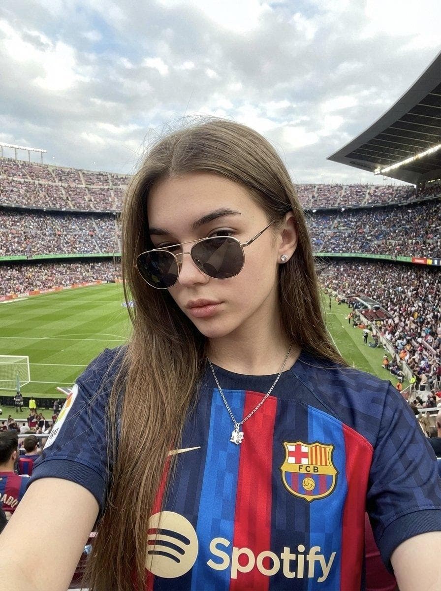 { "type": "image_generation_prompt", "language": "en", "style": "realistic smartphone photography, vibrant sports atmosphere", "aspect_ratio": "3:4", "identity_preservation": { "use_reference_image": true, "strict_identity_lock": true, "alter_face": false, "alter_features": false, "notes": "Use the uploaded reference photo. Preserve 100% of the woman’s facial features, proportions, skin texture, hair, and identity." }, "subject": { "gender": "female", "pose": { "type": "selfie-style pose", "orientation": "facing the camera", "action": "static moment, as if pausing to take a selfie" }, "expression": "serious, confident, and admiring", "appearance": { "hair": "unchanged from reference image", "accessories": [ "aviator-style sunglasses with gold frame", "diamond stud earring in the right ear", "silver chain necklace with a pendant" ] }, "wardrobe": { "top": "official FC Barcelona jersey with Spotify sponsorship" } }, "composition": { "framing": "centered composition", "foreground": "woman occupying the first plane", "background": "football stadium and crowd", "perspective": "first-person selfie perspective" }, "environment": { "location": "packed football stadium", "elements": [ "vibrant green football pitch", "crowded stands full of fans", "energetic stadium atmosphere" ], "weather": "cloudy sky", "mood": "excitement, celebration, pride" }, "lighting": { "type": "natural daylight", "conditions": "bright but diffused due to cloudy sky", "effects": [ "vivid colors", "balanced exposure", "clear facial details" ] }, "camera": { "device_style": "smartphone rear camera", "shot_type": "selfie-style medium close-up"…