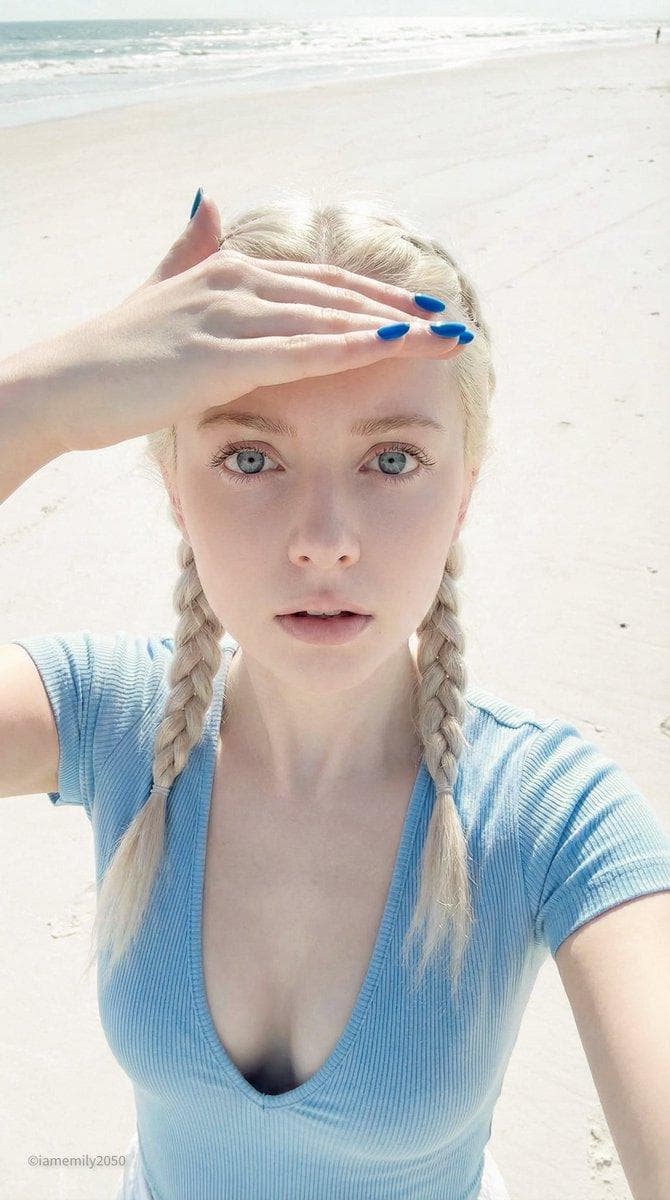 { "format": { "type": "editorial", "intent": "candid/selfie/accidental", "aspect_ratio": "9:16", "resolution": "4K" }, "camera_system": { "body": "iPhone 15 Pro", "lens": "Main Camera", "focal_length": "24mm", "associative_traits": "computational photography, deep depth of field, sharp digital readout, auto-exposure" }, "subject": { "identity": "young woman with specific porcelain doll features", "physical_details": "flawless pale skin, large round icy blue eyes with defined lashes, small defined nose, pouty neutral mouth, platinum blonde hair in two tight braids, vibrant blue manicured nails", "clothing": "light blue form-fitting top with a very deep, wide plunging V-neckline revealing significant cleavage", "action": "high-angle selfie POV, shielding eyes with one hand against bright coastal light, looking up at camera", "expression": "neutral, wide-eyed, deadpan, vacant doll-like stare" }, "lighting": { "source": "bright natural coastal daylight + sand bounce", "direction": "overhead and omnidirectional fill", "quality": "soft, diffused but very bright", "color_temp": "neutral daylight (5500K)", "fill": "maximum fill from bright white sand reflection", "distribution": "even illumination, few shadows, flattering on skin texture", "intent": "bright beach day" }, "environment": { "setting": "sandy beach during the day", "hero_materials": [ { "material": "sand", "micro_detail": "fine white grains, highly reflective" }, { "material": "fabric", "micro_detail": "light blue swimwear/stretch cotton blend" }, { "material": "skin", "micro_detail"…