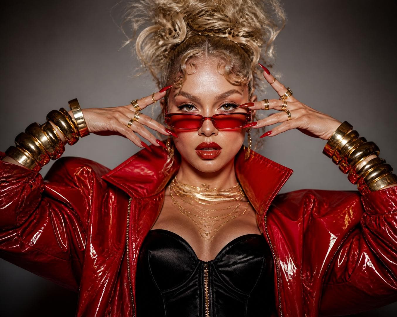 Ultra high-fashion editorial portrait of a striking young blonde woman, waist-up composition, powerful dominant pose, chin slightly lifted, piercing confident gaze directly into the camera lens, parted glossy plump lips with bold vibrant red wet-look gloss reflecting studio lights.Sculptural cheekbones with glowing dewy skin, luminous highlighter on cheekbones, nose bridge and cupid's bow.HAIR: dramatic voluminous curly blonde hair sculpted into an architectural high updo with rebellious loose tendrils flowing around the face, baby hairs laid in artistic swirls on the temples, glossy hair finish catching cinematic light.ACCESSORIES: micro-narrow futuristic rectangular sunglasses with red tinted lenses in glossy red frame, slipped seductively down the nose bridge revealing intense eyes above the rim. Both hands raised symmetrically and elegantly framing the face, fingers spread with theatrical precision, showcasing oversized chunky polished gold cuff bracelets stacked on each wrist, plus multiple statement gold rings on every finger, long almond-shaped glossy red nails with chrome finish.WARDROBE: oversized couture patent-leather bomber jacket in vibrant glossy red with mirror-glossy wet finish, exaggerated power-shoulders, voluminous puffed sleeves cinched at the wrist, dramatic wide lapels popped up around the neck, golden chunky zipper pull catching highlights. Underneath — a sleek black silk corset top with subtle sheen. Delicate layered gold chain necklaces draping across the collarbones.BACKGROUND: seamless minimalist studio backdrop in warm dove-grey with subtle vignette gradient fading to deeper shadow at the edges, creating dramatic spotlight effect on the subject.LIGHTING: cinematic high-fashion beauty lighting setup — soft large octabox as key light creating…