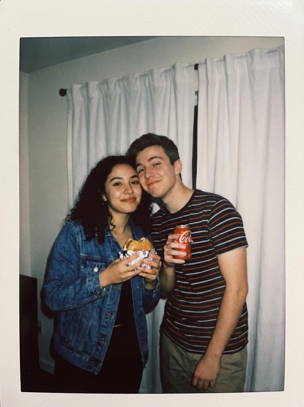 { "type": "image_generation_prompt", "style": "Polaroid-style candid photography", "camera_style": { "camera": "Polaroid instant camera", "look": "ordinary snapshot", "effects": [ "slight blur", "soft focus", "flash-lit dark room glow", "light scattering from on-camera flash", "subtle film grain", "slight exposure falloff" ] }, "identity_preservation": { "use_reference_images": true, "strict_identity_lock": true, "alter_face": false, "notes": "Do not change or distort either person’s facial features, expressions, or proportions." }, "subjects": [ { "gender": "female", "identity": "user", "pose": "cute, casual pose standing close to the boy", "prop": "holding a burger", "expression": "natural, playful, candid" }, { "gender": "male", "identity": "boy from reference", "pose": "cute, relaxed pose next to the girl", "prop": "holding a red Coca-Cola can", "expression": "natural, playful, candid" } ], "interaction": { "relationship": "friendly and cute", "body_language": "standing close together, relaxed, slightly leaning toward each other" }, "environment": { "background": "plain white curtains", "location": "indoor room", "lighting": { "type": "single on-camera flash", "quality": "consistent, frontal flash lighting", "mood": "cozy, intimate, nostalgic" } }, "composition": { "framing": "medium shot", "angle": "eye-level", "balance": "centered, casual snapshot composition" }, "aesthetic": { "vibe": "cute…