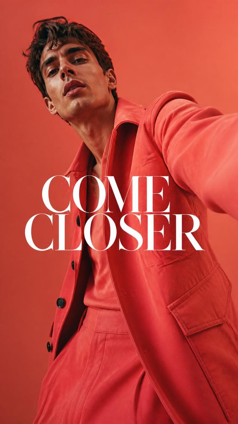 Luxury fashion editorial. Main Subject: Male model wearing a vivid coral jacket. Pose: One shoulder leaning toward the camera creating asymmetry. Camera: 24mm dramatic…
