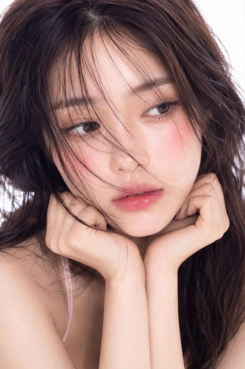 Ultra-realistic cinematic beauty portrait of a young Korean woman, soft dewy glass skin, natural pink blush, glossy gradient lips, delicate freckles, wispy messy bangs partially covering face, long dark flowing hair moving in the wind, dreamy innocent expression, detailed brown eyes with soft catchlight, pastel Korean makeup, wearing a light pink spaghetti strap top, high-end beauty editorial photography, photorealistic skin texture, luxury skincare campaign aesthetic, soft cinematic lighting, shallow depth of field, 85mm lens, f1.4, HDR, ultra detailed, 8k masterpiece quality, clean white studio background, soft diffused lighting, minimal elegant composition. Ultra-realistic outdoor portrait of a young Korean woman standing on a sunlit forest road, long dark brown hair blowing naturally in the wind, soft flushed cheeks, glossy lips, natural glass skin, wide expressive eyes, dreamy…