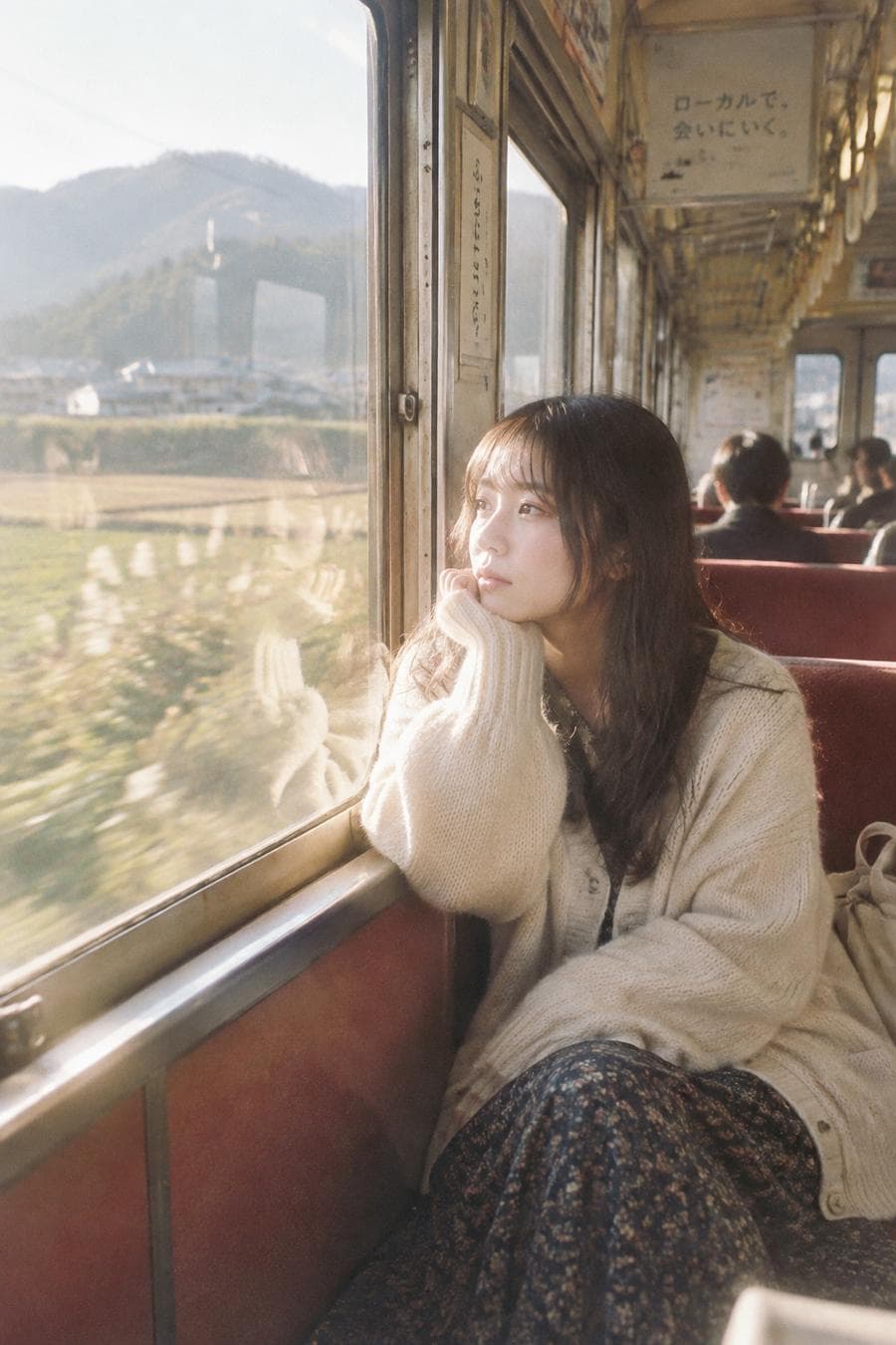 A beautiful Japanese woman sitting beside the window inside an old local train crossing the countryside, oversized cream cardigan, long skirt, softly resting her chin on her hand while watching the passing scenery, warm afternoon sunlight washing across the train interior, subtle reflections on the glass, ordinary everyday moment, candid documentary photography, accidental framing, soft motion blur outside the window, Kodak ColorPlus 200, Canon EOS Kiss, scanned…