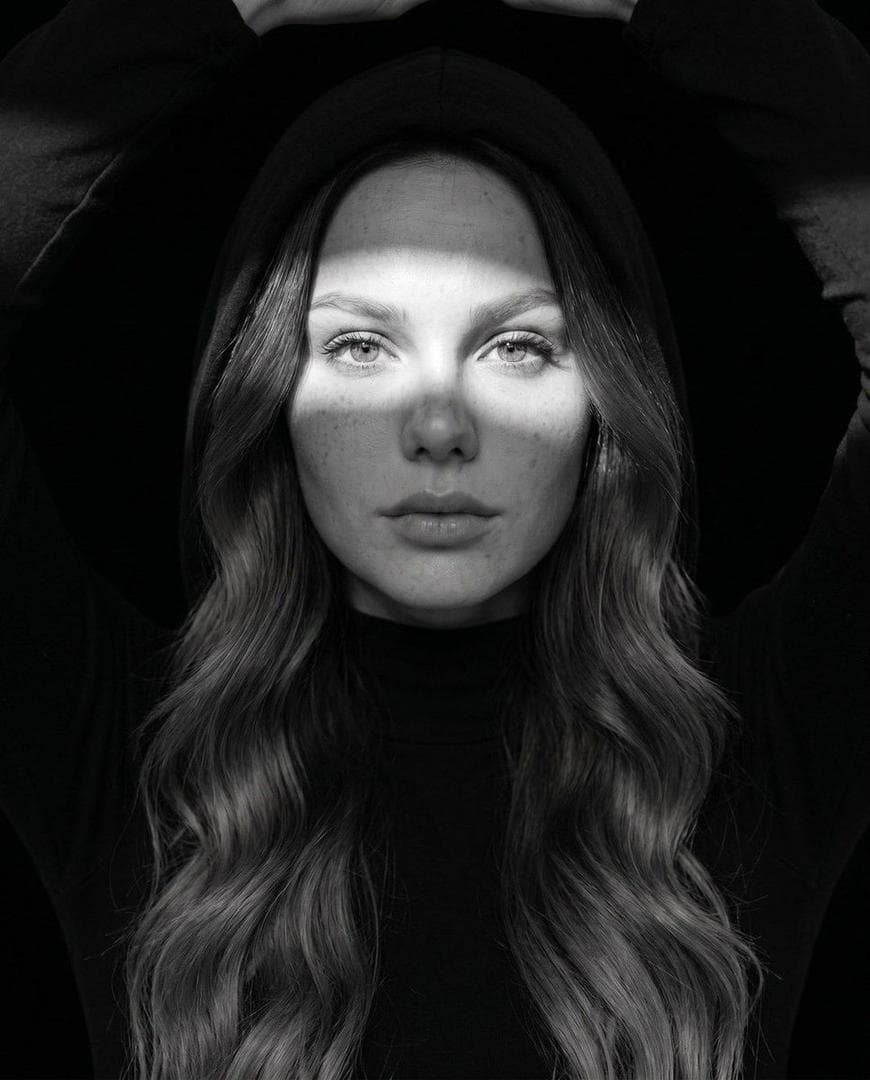 Ultra-realistic fine art black-and-white portrait, editorial fashion photography, close-up centered composition, direct eye contact, calm yet emotionally powerful expression, flawless natural skin texture with subtle freckles and pores, cinematic high-contrast monochrome grading, dramatic Rembrandt lighting with soft directional light, deep blacks and luminous highlights, razor-sharp eyes with catchlights, premium medium-format camera quality, 85mm portrait lens, f/1.8, shallow depth of field, museum-quality fine art photography, minimalist composition, timeless elegance, luxury Vogue-style editorial, rich tonal range, ultra-detailed facial features, photorealistic, HDR, 8K resolution, award-winning portrait photography. Variation 1 (Underwater): Half-submerged underwater portrait, crystal-clear water surface crossing the forehead, natural water caustic light patterns dancing across the face and shoulders, floating hair, tiny air bubbles, soft underwater haze, blurred fish in the distant background, tranquil atmosphere, surreal yet realistic, monochrome fine-art aesthetic. Variation 2 (Studio Hood): Black hooded outfit against a pure black background, narrow beam of light…