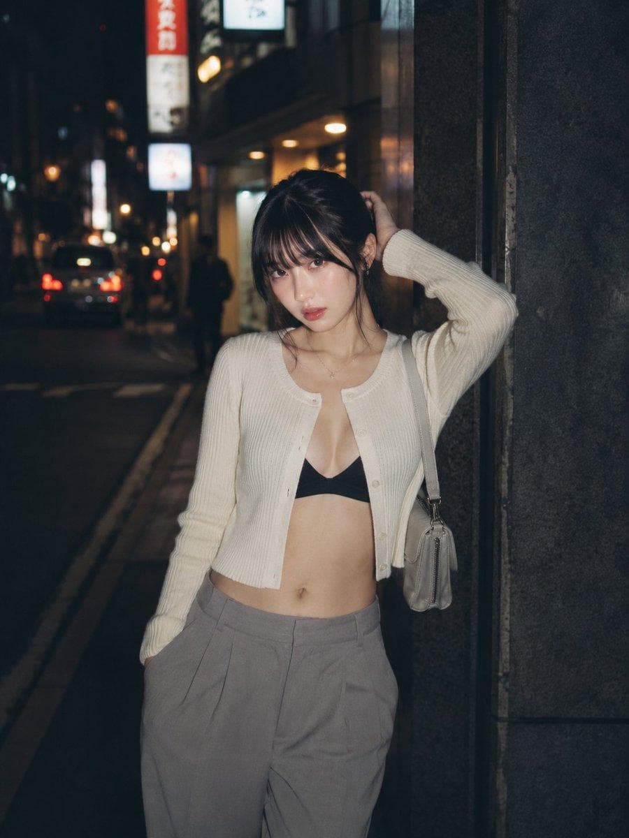主題：夜路地 人物・表情： 20代女性。幼さのない自然で成熟した雰囲気。黒茶色のミディアムヘアをゆるくまとめ、薄い前髪と顔まわりの後れ毛を残す。清透な日系写真メイク、自然な肌の質感。唇は控えめな血色感。顔を少し傾け、カメラをまっすぐ見る落ち着いた表情。 服装・ポーズ： 白〜アイボリーの細リブニットカーディガンを前開き気味に着る。インナーは黒のシンプルなブラトップ、下はグレーのハイウエストワイドスラックス。小さなライトグレーのショルダーバッグを片肩にかける。身体は画面左へ少し傾け、背中を暗い石壁に軽く寄せる。人物自身の左手を後頭部に添え、右手はパンツのポケットに入れる。指先は自然に曲げ、肩と腰にゆるい重心差をつける。上品で控えめな大人の街頭ポートレート。 背景・光： 東京の夜の裏通り。暗いビル壁、細い歩道、奥にぼけた車のテールランプ、看板灯、街灯の丸い光。背景の文字は読めない程度にぼかす。路面は少し湿っていて、街灯の反射が細く伸びる。人物の正面やや左上から弱いフラッシュのような白い光が当たり、顔、白いカーディガン、肩まわりを浮かび上がらせる。背景は深く沈み、奥の光だけが暖色のボケになる。 構図・カメラ： 縦構図 4:5。腰上から太もも上まで入るミディアムショット。人物は画面右寄りに配置し、左側に夜道の奥行きと暗い余白を残す。カメラは胸元より少し高い位置からほぼ平視。人物との距離は近めで、背景は浅めにぼかす。スナップ写真のような自然な距離感。焦点は瞳と顔まわり。…