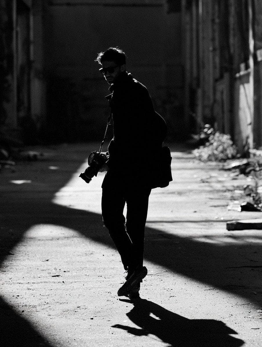 [Subject], black and white high contrast, harsh midday sun creating graphic shadow shapes across the body and ground, no fill light, blown highlights and crushed blacks, the image reading almost as shape and…