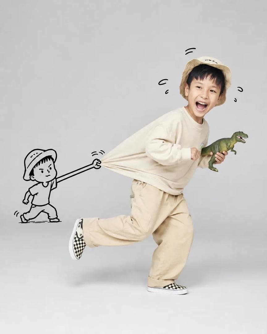 A playful, high-key studio portrait of [Subject] running joyfully across a seamless light gray background, captured mid-stride with one leg lifted and a wide genuine smile. The subject wears a casual oversized outfit with soft neutral tones (or vibrant colors), creating a dynamic sense of motion. Behind them, a simple black hand-drawn cartoon stick figure grabs and stretches the back of their shirt, making the fabric appear elastically pulled as if trying to stop them. The doodle character is integrated naturally into the scene with expressive motion lines and a humorous facial expression. The subject holds a fun prop (such as a dinosaur toy, oversized lollipop, teddy bear, or…