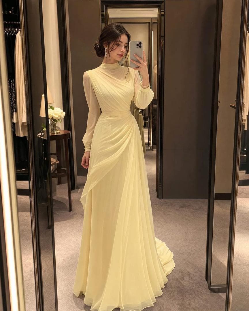 Ultra-realistic full body mirror selfie of a beautiful young woman wearing a soft pastel butter-yellow luxury evening gown inspired by high-fashion couture. Elegant full-length gown with modest sophisticated design, flowing layered chiffon fabric, refined draped silhouette, high neckline, long sheer-lined sleeves, fully covered bodice, floor-length skirt with no slit, graceful A-line shape, luxurious couture craftsmanship, feminine and classy silhouette. Fabric remains soft, premium, and richly textured with delicate ruching and elegant draping. Hair styled in a sleek low bun, ultra neat and elegant with glossy dark brown hair, soft face-framing strands. Korean beauty makeup look: glowing glass skin, soft peach blush, subtle contour, glossy nude lips, long wispy lashes, natural aegyo-sal eyes, dreamy feminine expression. Pose: classy mirror selfie, holding phone naturally, standing confidently, full body visible from head to toe. Elegant luxury boutique fitting room background with warm cinematic lighting, fashion runway atmosphere, reflective mirror, soft shadows, expensive couture vibe. Accessories: delicate diamond earrings…