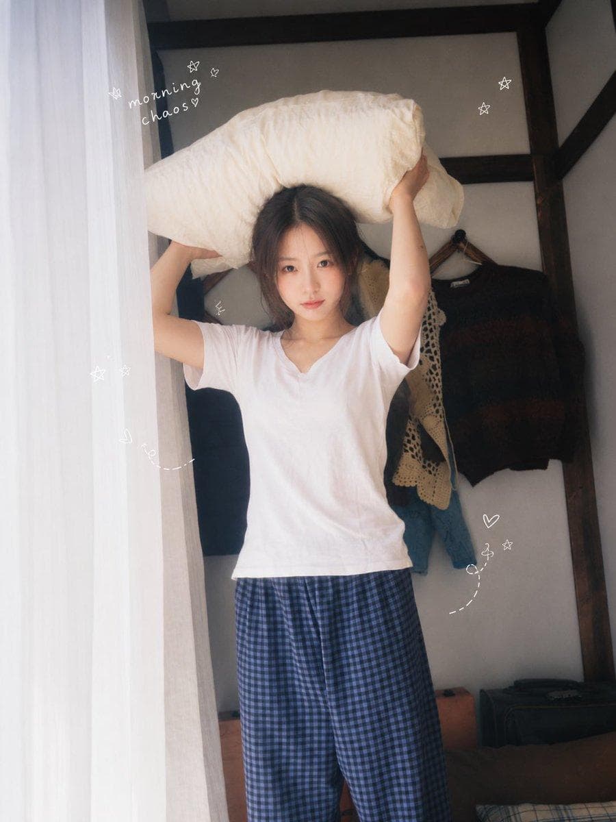一位二十多岁的年轻东亚女性,黑色长发随意扎成低马尾,几缕碎发自然垂落,淡妆,真实自然的皮肤纹理,眼神清澈,表情慵懒又俏皮。她穿着宽松白色短袖T恤和蓝黑色格纹居家长裤,在温馨复古的小卧室里度过悠闲周末。 室内有蓝白格纹床品、木质家具、复古衣架、布艺沙发、旧报纸、早餐餐桌、面包和玻璃杯。人物做自然生活化动作:抱着枕头、趴在床上托腮、躺在沙发上发呆、举着中间挖成爱心形状的吐司、伏在桌前写字、倒躺在床上遮住半张脸。每张图片使用不同动作、视线和微表情,不要重复僵硬姿势。 窗边柔和自然晨光,白色纱帘透光,低饱和奶油色与蓝色调,清新日系居家写真,韩系生活杂志感,真实随拍构图,轻微俯拍与广角透视,浅景深,柔和高光,细腻胶片颗粒,轻微朦胧感,旧数码相机与35mm胶片质感,温暖、安静、松弛、治愈。…