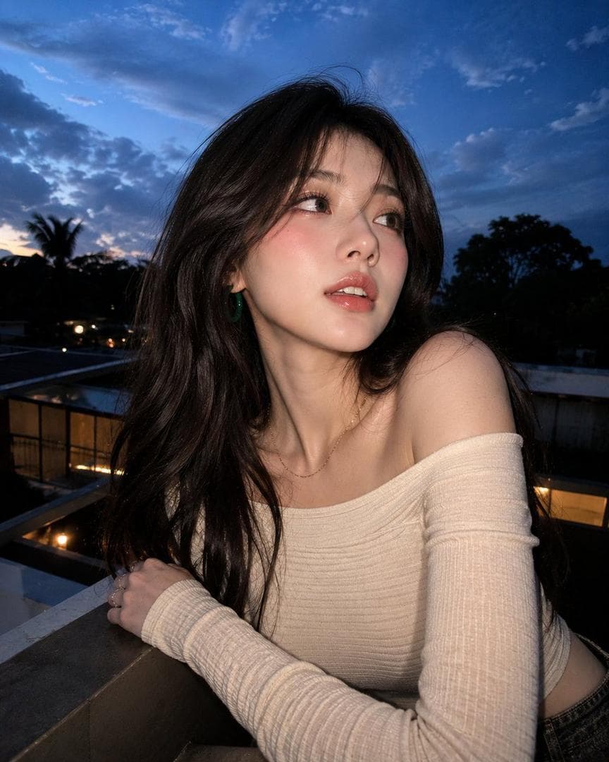 Reference Face: 100%, no alternation, no modification facial features, just keep it exactly as they are), Generate an ultra-realistic, highly ultra-detailed, 8k resolution, true-to-life portrait of a young woman in her 20s.8 Clothes Wearing: A fitted, ribbed, long-sleeved off-the-shoulder top in a creamy white or pale beige color. The fabric has a distinct horizontal ribbing texture. The neckline is wide and straight (boat neck style), fully exposingthe collarbones and shoulders. She is wearing a delicate, thin gold chain necklace and a chunky green hoop earring visible on her left ear. The Background: An outdoor setting at dusk or early evening featuring a deep blue sky scattered with wispy white clouds. In the lower background, there are silhouettes of trees (possibly palm or tropical) and a building railing or roofline, suggesting a rooftop or balcony environment.The Pose Setting: A high-angle selfie shot where the subject is looking away from the lens, glancing upward and to her right with a candid, spontaneous expression. Her mouth is slightly parted in a natural, relaxed manner, showing her teeth. The angle suggests she is holding the camera with an…