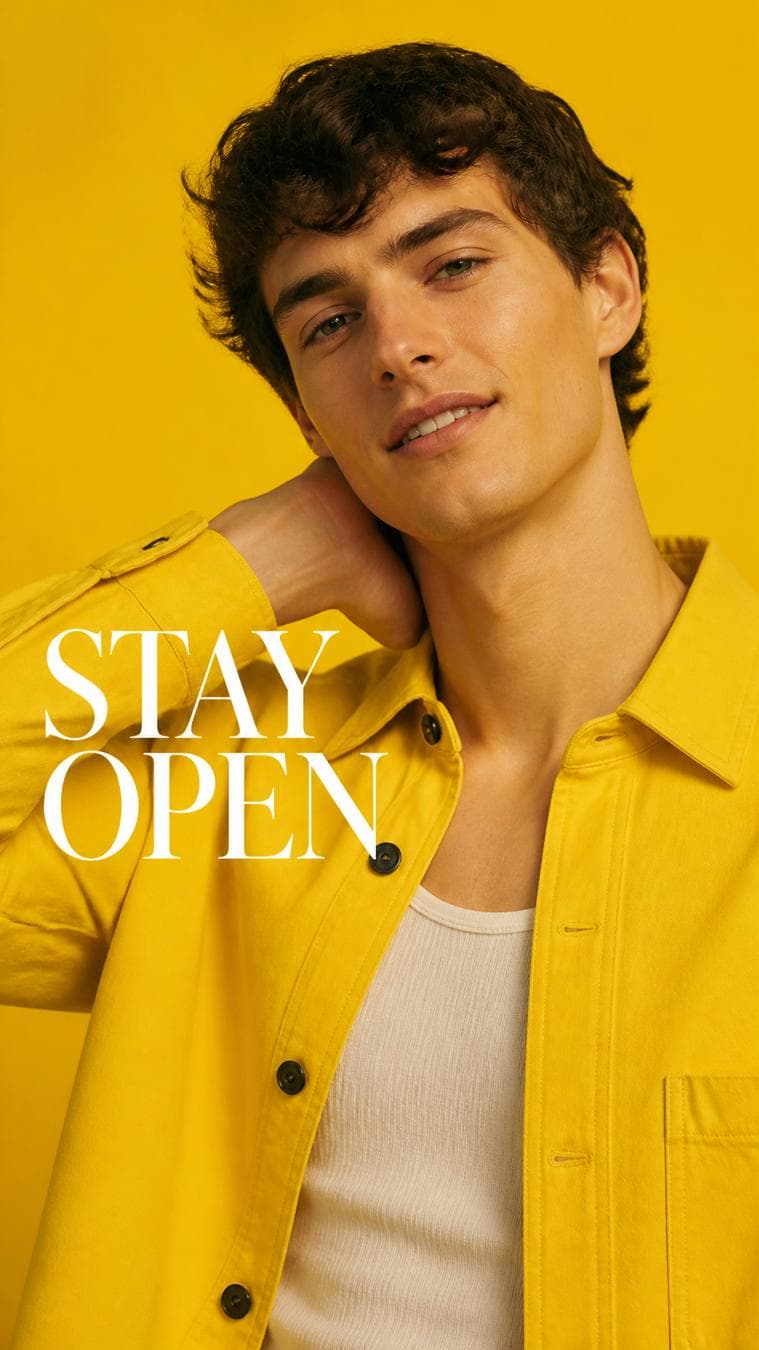Premium fashion campaign. Main Subject: Young male model wearing a bright sunflower-yellow overshirt. Pose: Holding the back of his neck while smiling slightly. Camera: Tight portrait with natural…