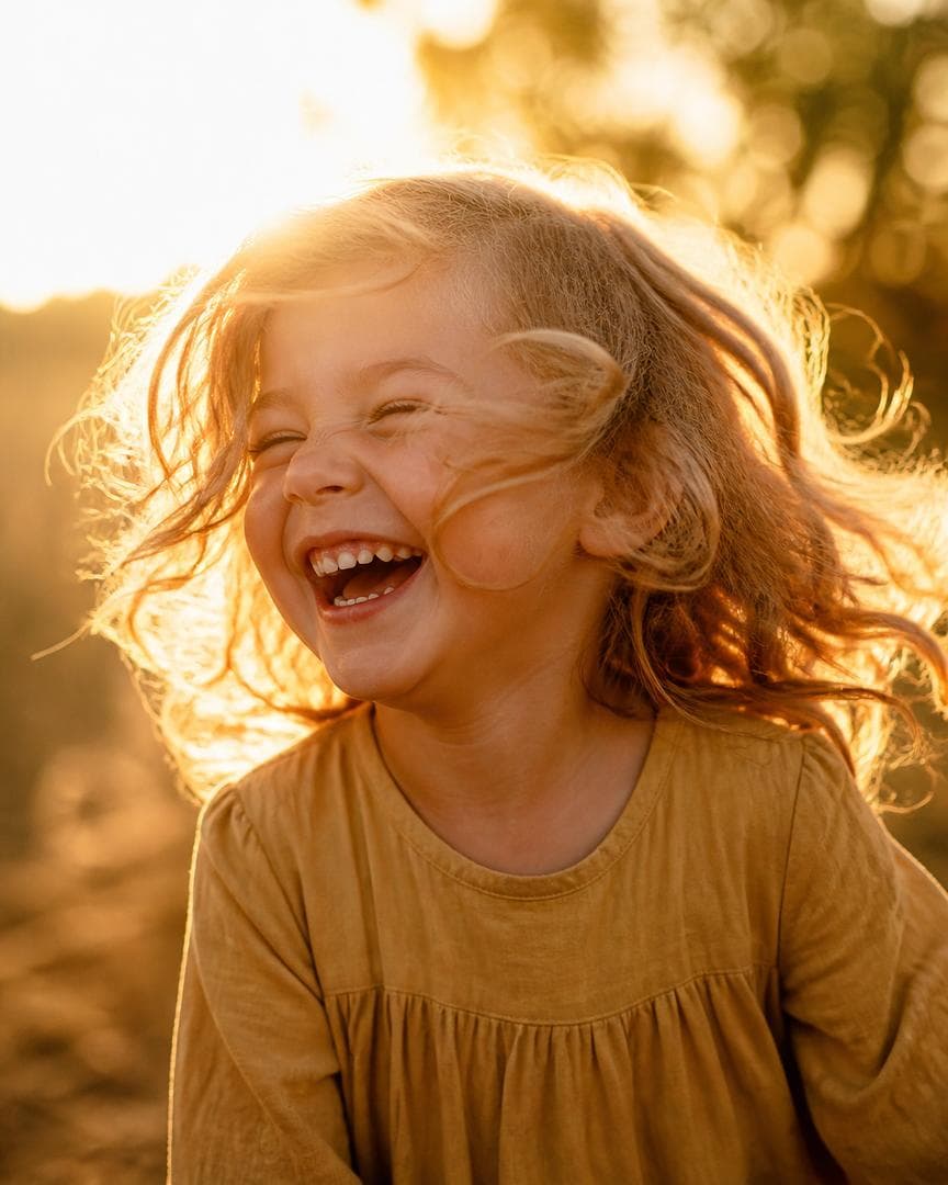 Create a hyper-realistic editorial portrait of a young child laughing with pure joy, eyes squinting, mid-motion with windswept hair, golden afternoon light. FORMAT: 4:5 vertical, tight editorial crop. LIGHTING: warm golden backlight, glowing rim on the hair, soft natural skin texture. STYLE…